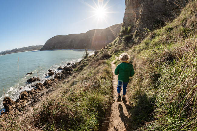 Vorschulkind läuft an sonnigem Tag in Neuseeland auf Bergpfad am Meer — Stockfoto