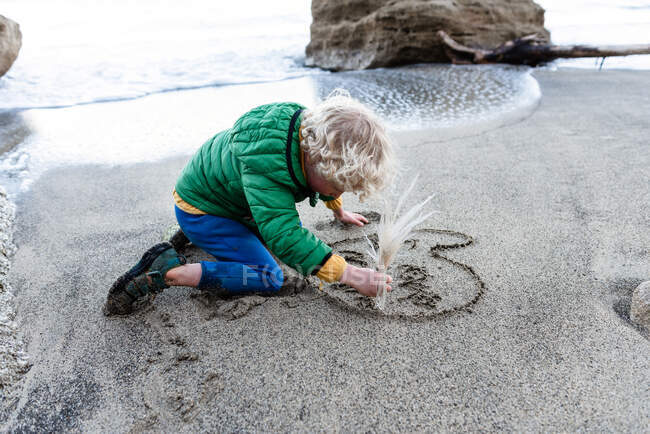 Kleines Kind schreibt Ich liebe Mama im Sand an einem Strand in Neuseeland — Stockfoto