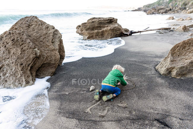 Kleines Kind schreibt im Sand am Strand in Neuseeland — Stockfoto