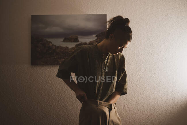 Androgynous woman tucks shirt in front of artwork in home at night — Stock Photo