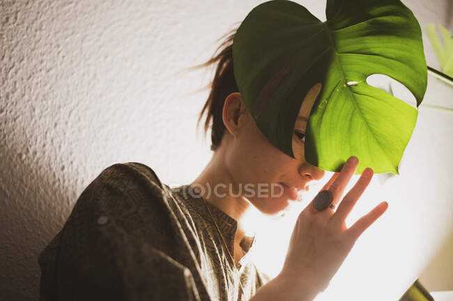 Азиатская женщина достигает пика через листья растений в лампе света дома — стоковое фото