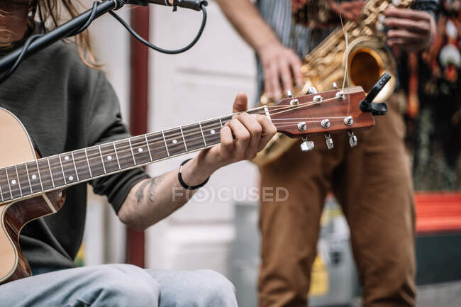 Musicien jouant de la guitare au milieu de la rue devant un microphone et avec un saxophoniste — Photo de stock