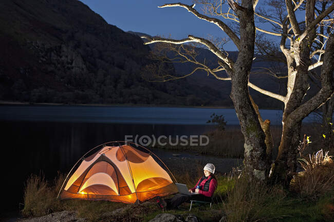 Mujer excursionista mirando su portátil en el campamento en el norte de Gales - foto de stock
