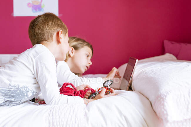 Two brothers lying in bed using the tablet — Stock Photo