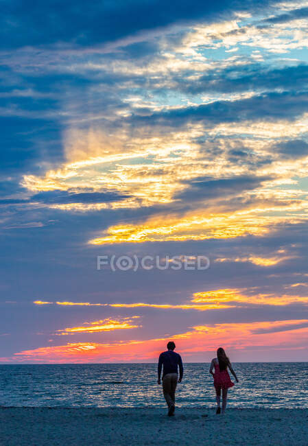 Jovem casal caminhando em direção ao oceano ao pôr do sol colorido — Fotografia de Stock