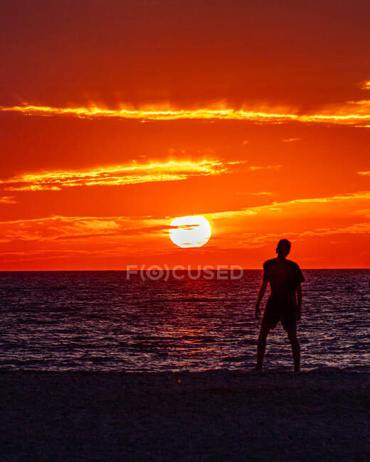 Boy watching sun set along the ocean shoreline admiring the fire sky. — Stock Photo