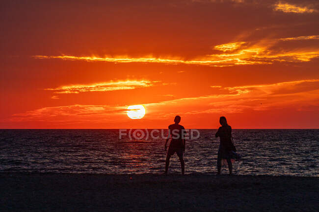 Junges Paar geht bei Sonnenuntergang am Strand entlang — Stockfoto