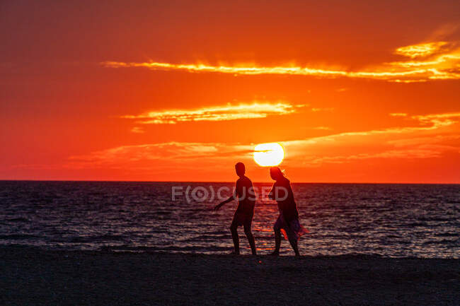 Jeune couple marchant le long de la plage au coucher du soleil — Photo de stock