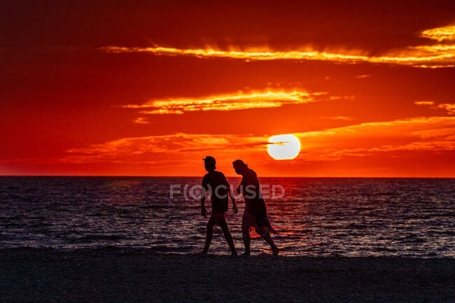 Jeune couple marchant le long de la plage au coucher du soleil — Photo de stock