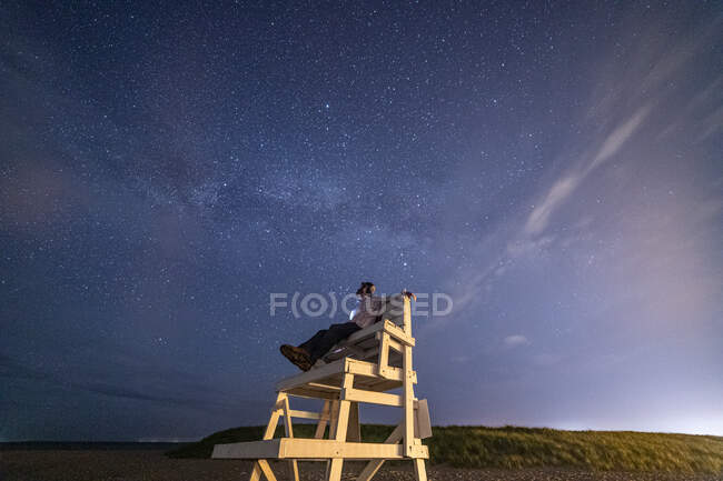 Homem sentado na cadeira salva-vidas admirando milkyway e estrelas acima. — Fotografia de Stock