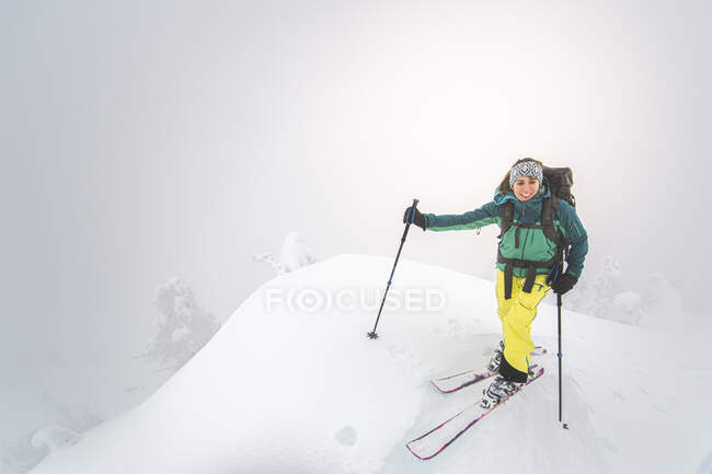 Young woman smiling backcountry skiing on snowy summit in Squamish — Stock Photo