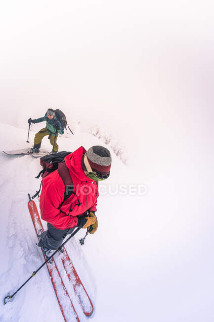 Two people backcountry skiing arriving at summit in the mist — Stock Photo