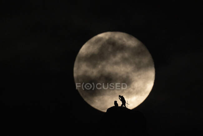A couple of climbers setting a rope with full moon in the background — Stock Photo