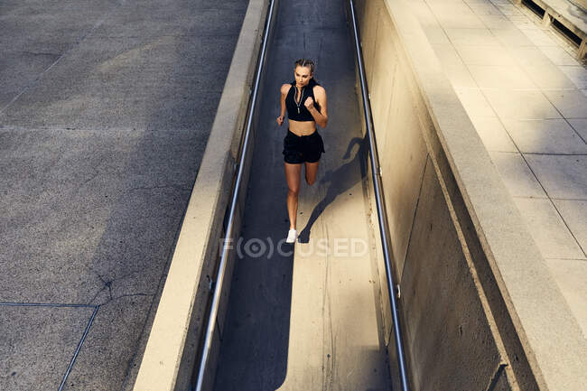 Retrato de hermosa mujer joven en ropa deportiva moderna con estilo corriendo en la calle de la ciudad - foto de stock