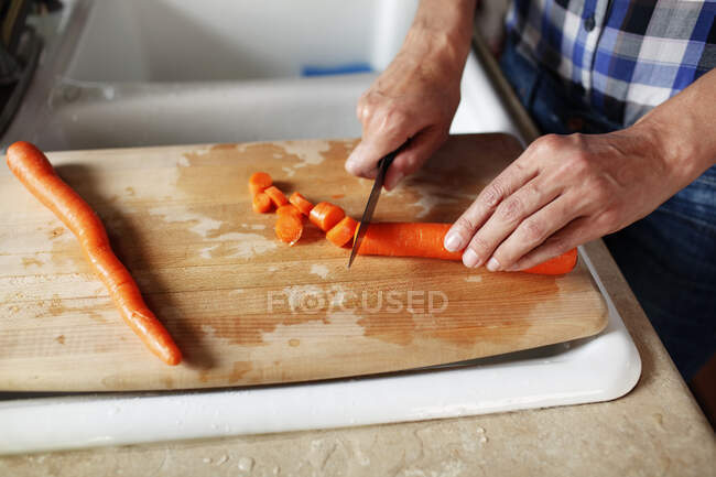 El primer plano de las manos de mujer cortando una zanahoria en un bloque de cortar - foto de stock
