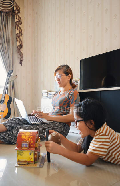 Uma menina está brincando nas proximidades de uma mãe que está trabalhando com um laptop — Fotografia de Stock