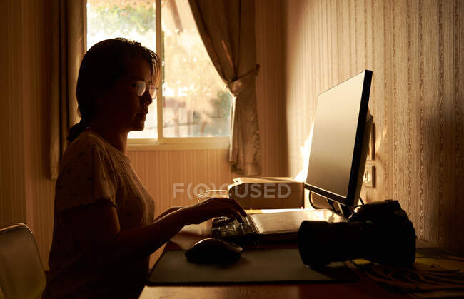 Una mujer que trabaja en una computadora en una habitación llena de luz cálida de la mañana - foto de stock
