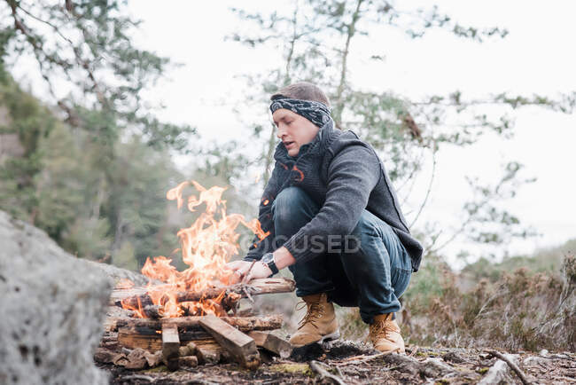Homme mettre des bâtons sur un feu de camp en plein air en Suède — Photo de stock