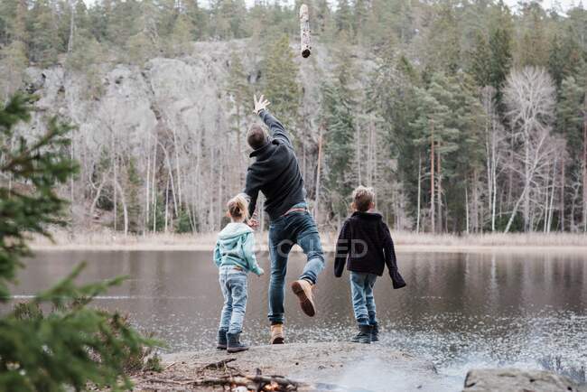 Vater wirft Baumstämme beim Wandern mit seinen Kindern ins Meer — Stockfoto