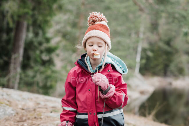 Menina comendo marshmallows por uma fogueira na floresta na Suécia — Fotografia de Stock