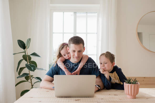 Pai trabalhando em casa com crianças subindo nele — Fotografia de Stock