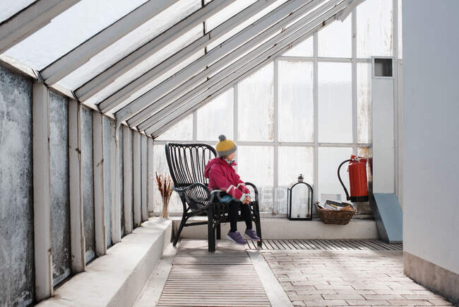 Mädchen sitzt im Winter auf einem Stuhl in einem Gewächshaus — Stockfoto