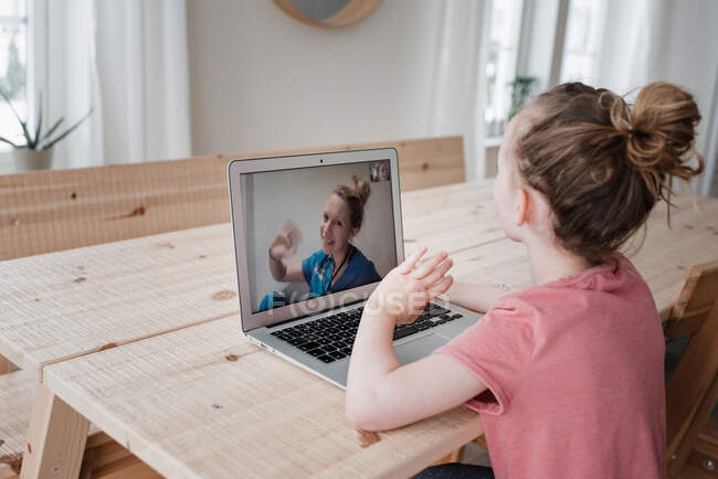Fille assis parler et saluer une infirmière sur un appel vidéo à la maison — Photo de stock