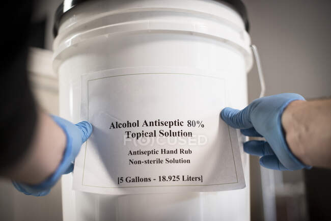 Un destilador pone la etiqueta en un cubo de desinfectante de manos. - foto de stock