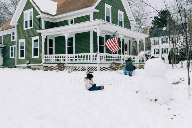 Ein Vater und seine Kinder basteln gemeinsam einen großen Schneemann im Vorgarten. — Stockfoto
