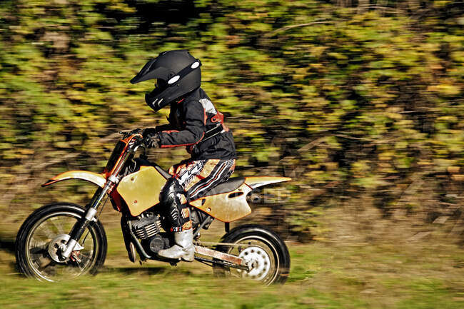 12-річний хлопчик їде на мотоциклі через поле. — стокове фото