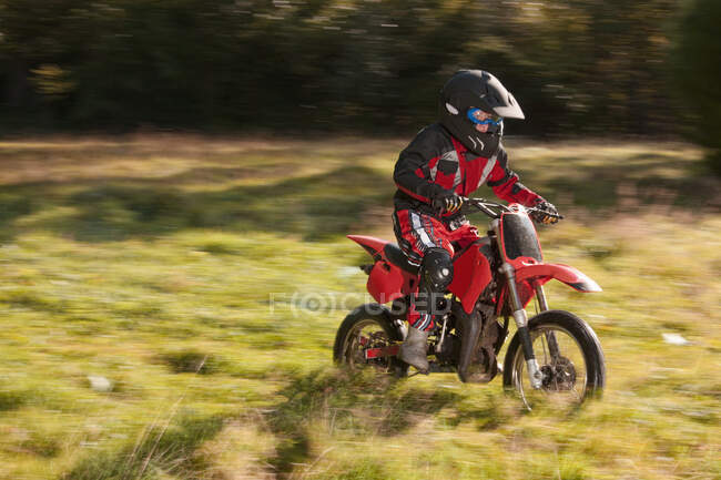 12 ans garçon chevauchant sa moto motocross à travers le champ — Photo de stock