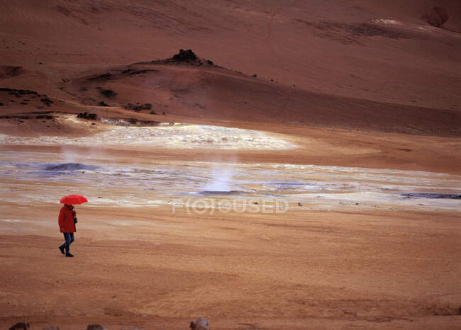 Женщина ходит с красным зонтиком в районе геотермальных источников Намскард — стоковое фото