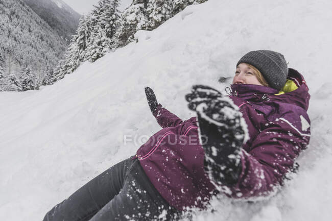 Jeune femme avec chapeau glissant rapidement dans la neige descente drôle visage — Photo de stock
