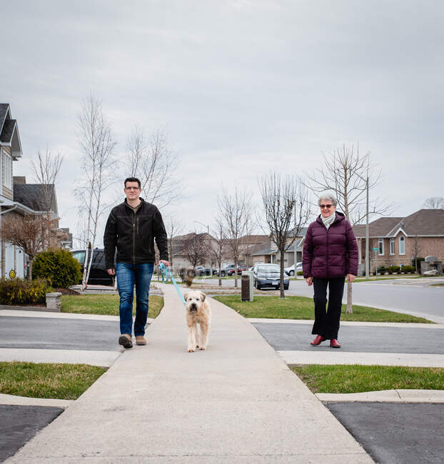 Man and older lady walking dog on sidewalk of suburban neighborhood. — Stock Photo