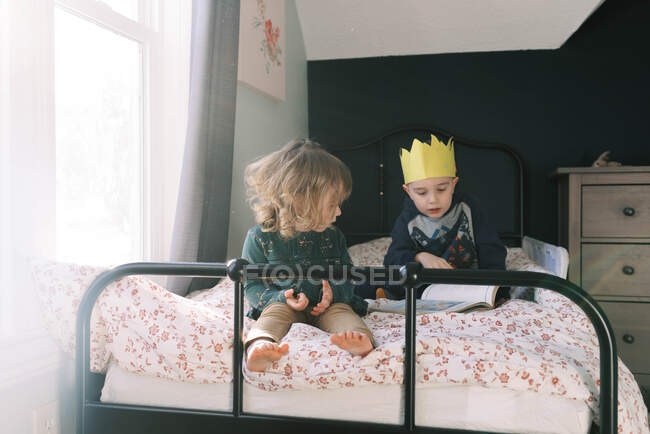 Братья и сёстры играют вместе на кровати и читают книги. — стоковое фото