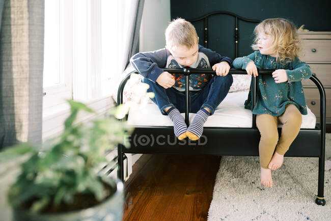 Irmãos brincando em uma cama juntos felizes enquanto na casa. — Fotografia de Stock