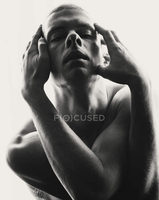 Schwarz-Weiß-Porträt eines hemdslosen Mannes, der das Gesicht unbeholfen berührt — Stockfoto