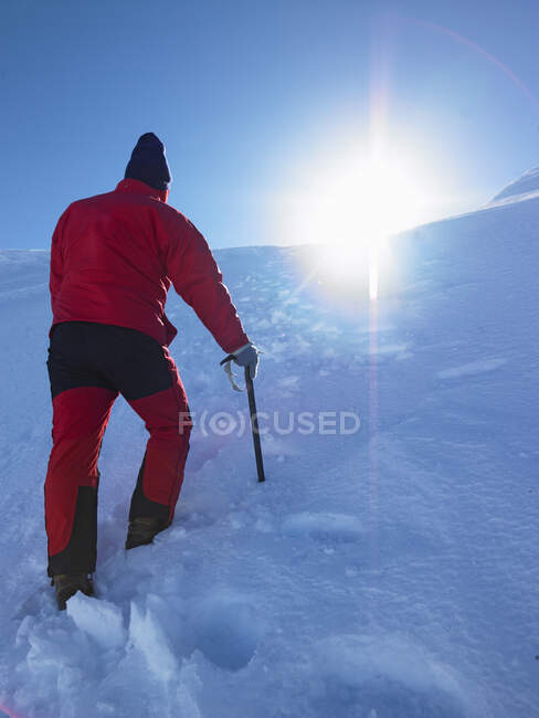 Homem caminhando para cima colina nevada em direção a um cume — Fotografia de Stock