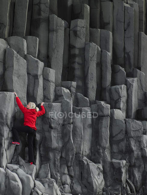 Mujer subiendo columnas de basalto en el sur de Islandia - foto de stock
