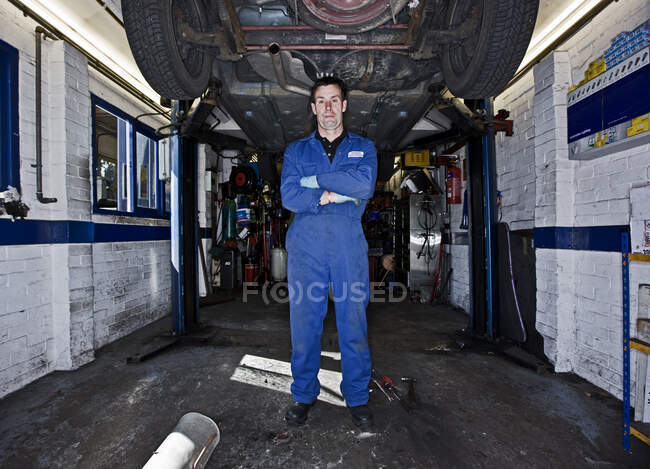 Car mechanic  posing under a car at automotive garage in the UK — Stock Photo