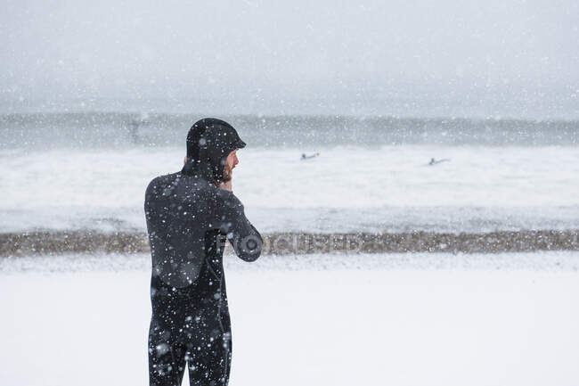 Man preparing to go surfing during winter snow — Stock Photo