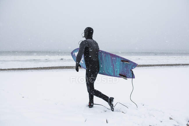 Man preparing to go surfing during winter snow — Stock Photo