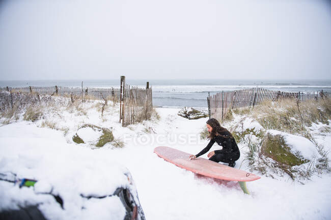 Mulher com uma prancha de surf na praia no inverno, Nova Inglaterra. — Fotografia de Stock