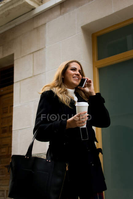 Mujer joven habla por teléfono mientras camina por la calle - foto de stock