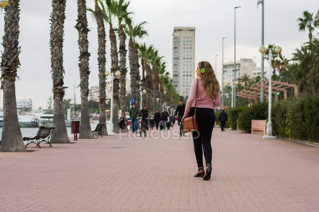 Молода жінка гуляє по вулиці слухаючи музику зі своїми навушниками — стокове фото