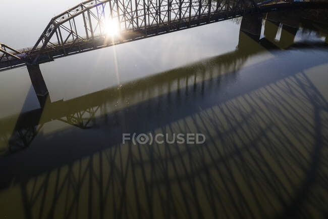 Puente proyecta sombra larga en el río durante la salida del sol - foto de stock