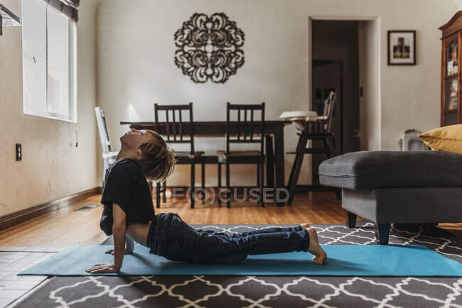 Young boy doing yoga in living room during isolation — Stock Photo
