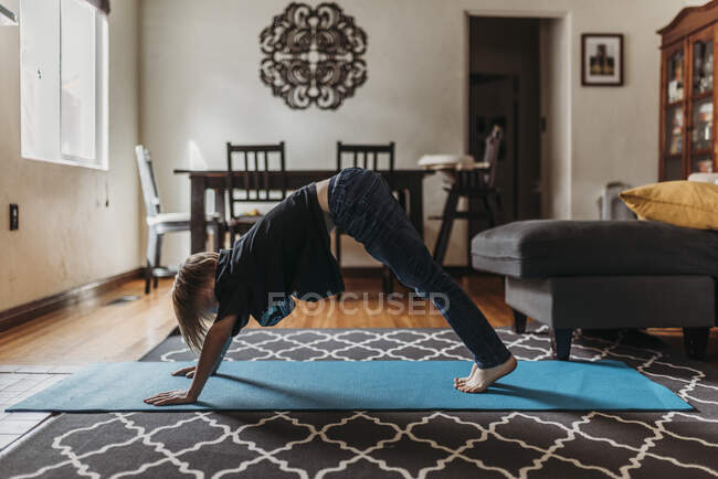 Niño haciendo yoga en la sala de estar durante el aislamiento - foto de stock
