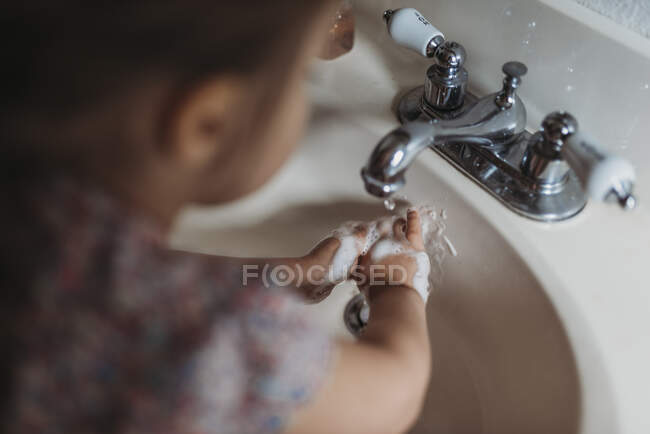 Маленькая девочка моет руки в раковине ванной с мылом. — стоковое фото