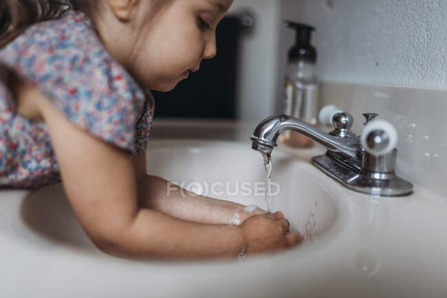 Petite fille se lave les mains dans l'évier de salle de bain avec savon. — Photo de stock